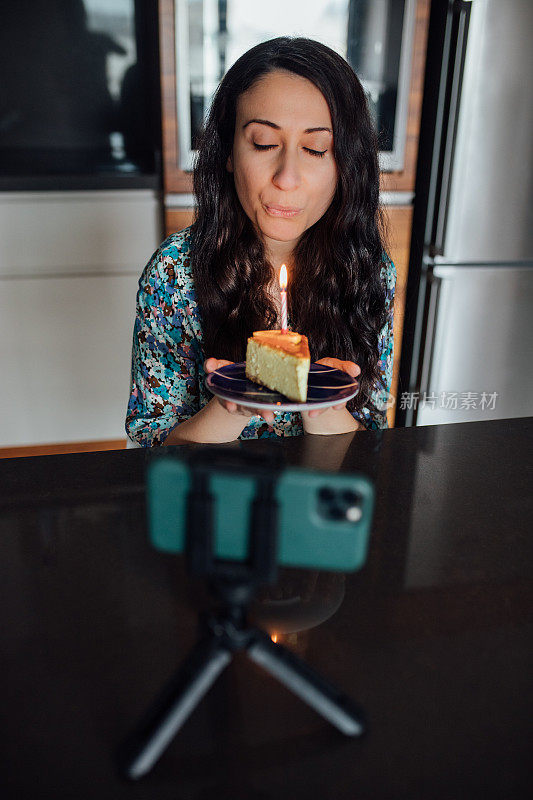 在家里和朋友视频会议时，手持蛋糕并吹灭蜡烛的女子
