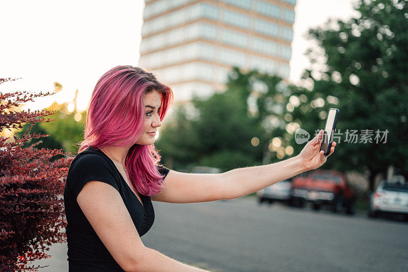 一个时尚的年轻女人的肖像与有趣的粉红色头发在户外在夏天自拍