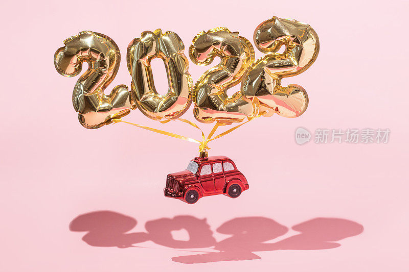 金色的2022年气球，红色的玩具车，粉红色的背景，五彩纸屑和圣诞节闪亮的球，平躺。新年庆祝理念