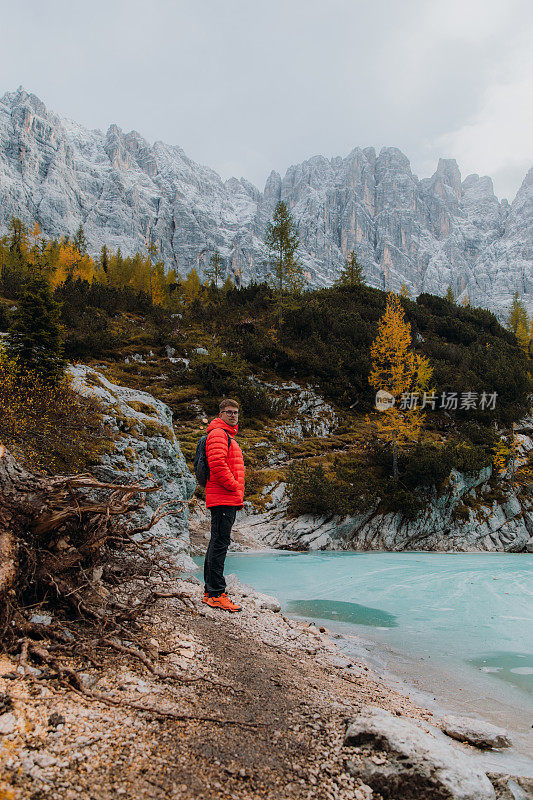 男旅行者呆在岩石上，凝视着阿尔卑斯山上冰封的高山湖泊的风景