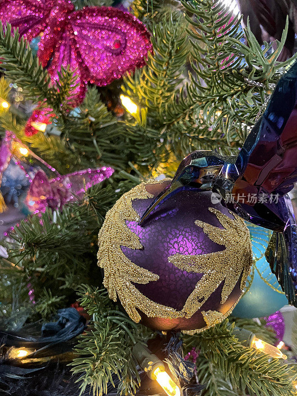 特写图像单个紫色的小玩意装饰着金色的闪光挂在人造圣诞树的树枝上，云杉针，模糊的白色精灵灯
