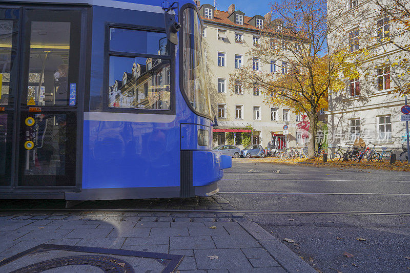 蓝色和白色的有轨电车在一个有汽车、树木和秋叶的城市设置