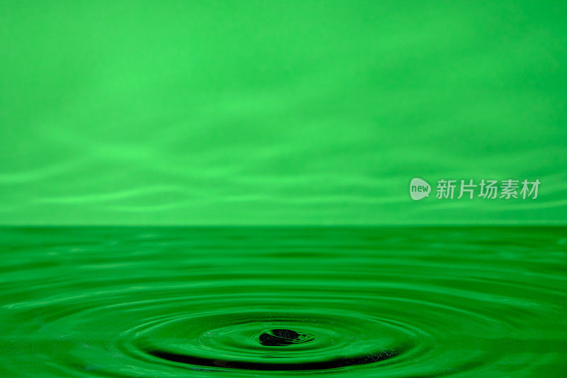 明亮的绿色背景与发散的圆圈从水滴表面的水。