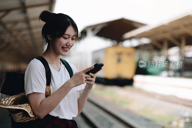 在背景轻轨站台上用智能手机等候的女子。旅客发短信并计划线路停靠铁路，铁路运输，预订。享受旅游的概念