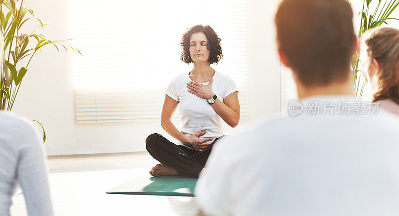瑜伽教练在健身教室里训练人们。瑜珈师教导呼吸调息技巧，双手放在胸部和腹部。练习正念冥想的禅能量在莲花姿势