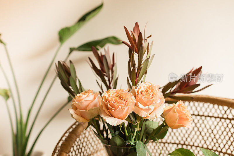 软桃色乡村玫瑰与锈色秋叶插在波西米亚藤椅上的花瓶里