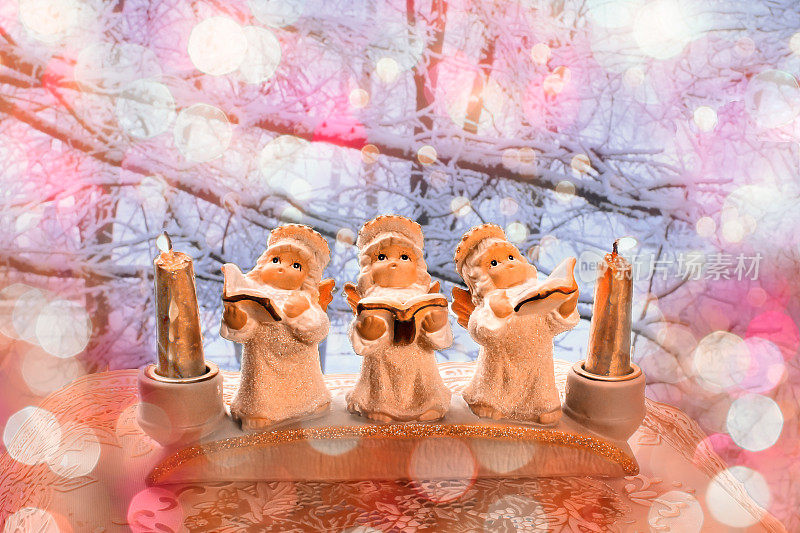 装饰三个石膏天使与蜡烛歌颂圣诞背景的冬季景观。一个贺卡