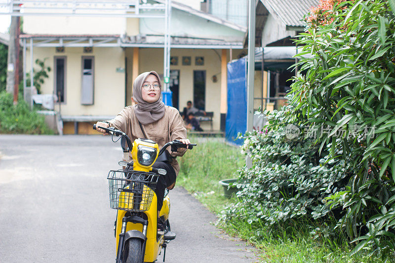 年轻的伊斯兰妇女在居民区骑电动自行车