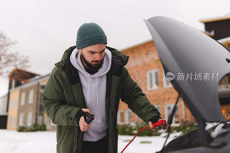 大胡子的年轻人在冬天的路边跳着启动他的汽车