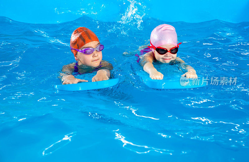 两个小女孩在泳池里玩得很开心，学习如何使用扑动板游泳
