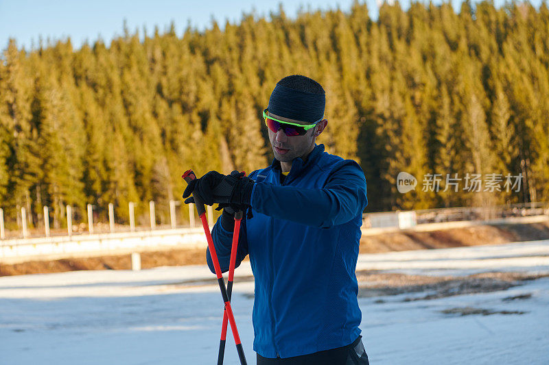 帅气的男运动员越野滑雪板，呼吸新鲜空气，在雪林艰苦训练后休息。检查smartwatch。健康的冬季生活方式