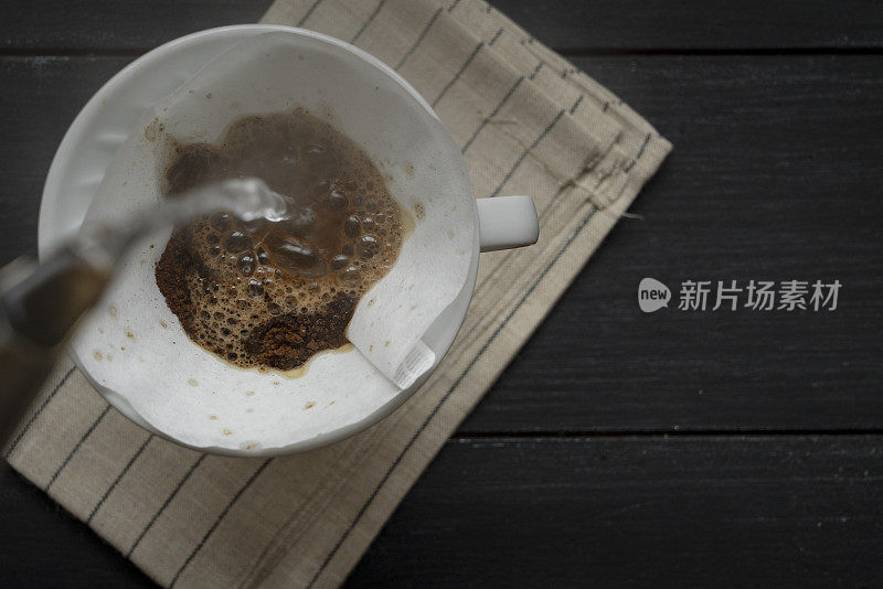 煮咖啡，把热水倒在杯子上的过滤器里的咖啡粉上，这是一种刺激的饮料，质朴的木桌