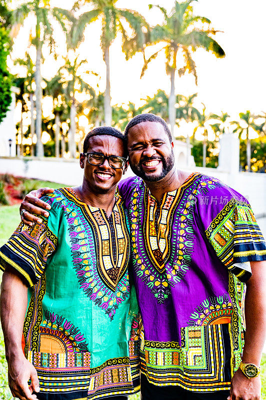两名成年男子穿着花哨的传统非洲服装，在户外快乐地摆姿势庆祝宽扎节