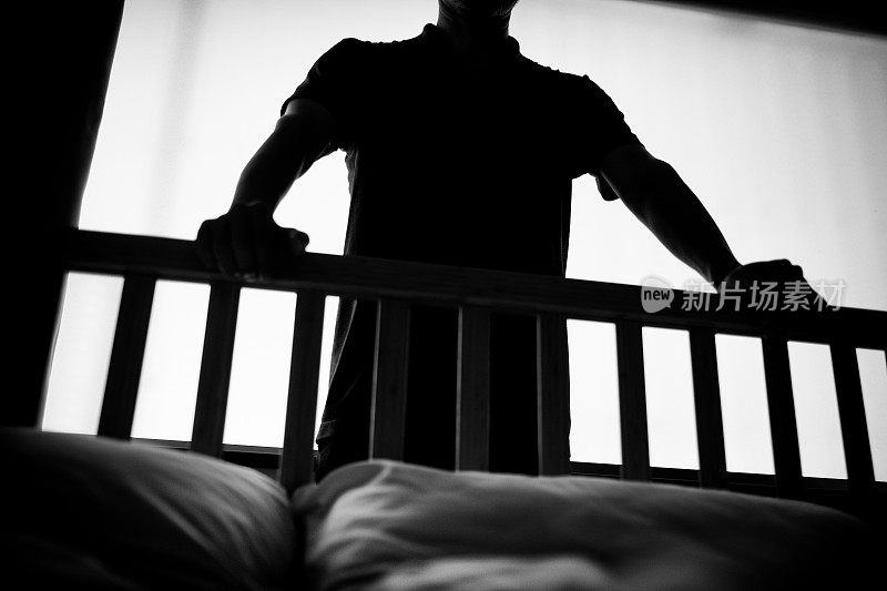 一个男人的剪影，他的手在床栏杆上向下看