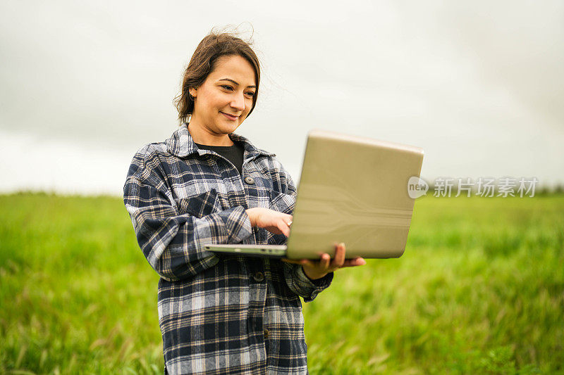 年轻的女农学家用装有智能农业应用程序的笔记本电脑控制着麦田