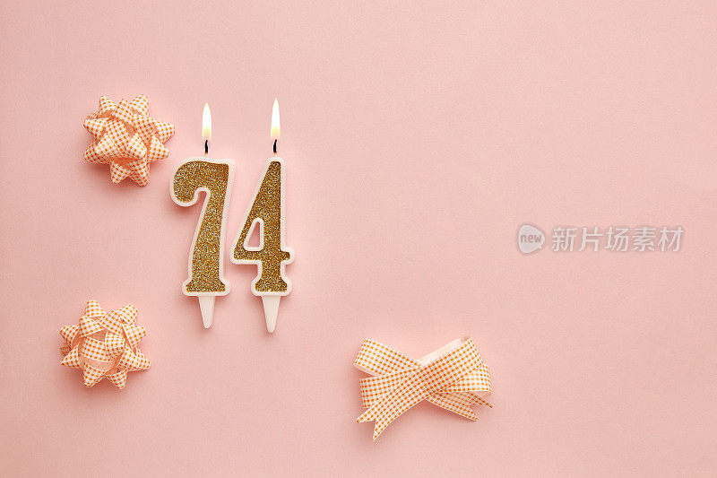 蜡烛与数字74在柔和的粉红色背景与节日装饰。生日快乐，蜡烛。庆祝生日、周年纪念、重要日期、节日的概念。副本的空间。横幅
