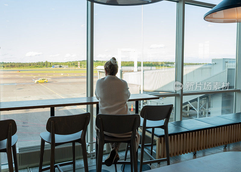 一位年轻的白人女子望着窗外的机场，在等待航班时梦想着度假。