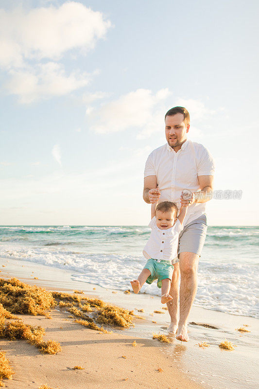 2023年春天，一位31岁的美国父亲和他第一次发现海滩的1岁儿子在海滩上玩耍，在佛罗里达州棕榈滩的金色日出期间一起享受时光