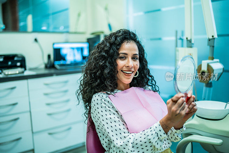 一个中年妇女在牙医诊所的镜子里看着自己的牙齿