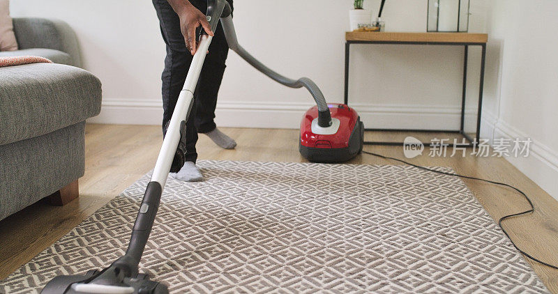 地毯，清洁和一个人用吸尘器在家庭休息室除尘，污垢和维护。带电器的吸尘器腿，在客厅里用吸尘器清扫房间