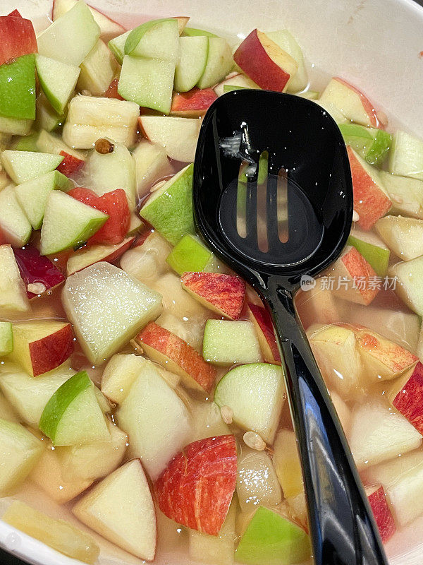 全画幅图片，白色的大碗新鲜水果沙拉，开槽的塑料勺子，切碎的绿色和红色的苹果在果汁中，健康的早餐替代品，高架视图