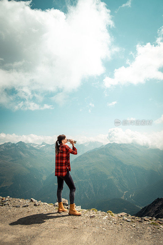 一个徒步旅行者站在那里，用保温瓶喝水，俯瞰着山谷。