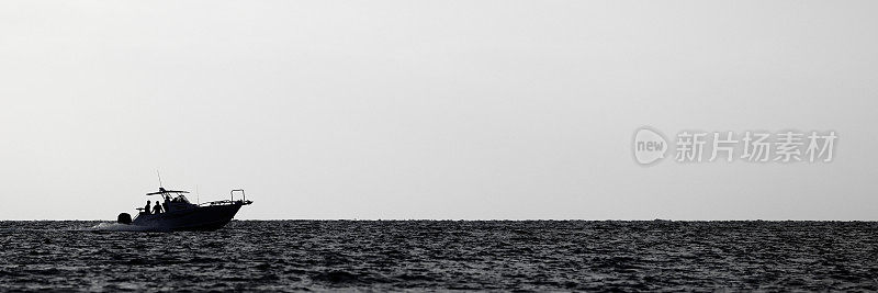 用于休闲钓鱼的摩托艇，在日落时返回港口。黑白照片，有足够的负片或复印空间。