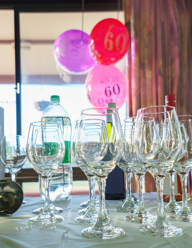 60岁生日的气球挂在窗户上，选择性地聚焦在桌子上的酒杯上。生日庆祝活动。垂直格式。