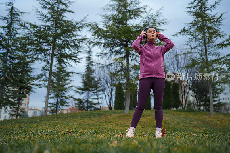 年轻女子戴着无线耳机，晚上在公园户外锻炼。