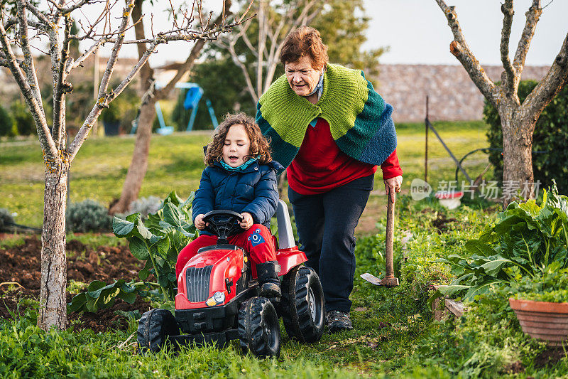 奶奶和孙子在家里的花园里玩拖拉机