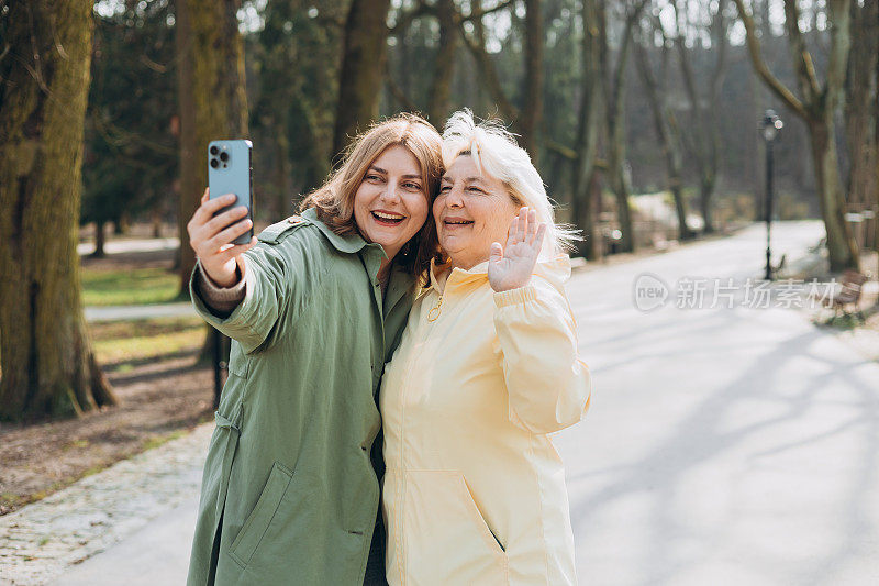 快乐的老母亲和成年女儿在城市街道上自拍。穿着得体的女性朋友户外照。两个女人在一起用手机自拍。家庭日概念。