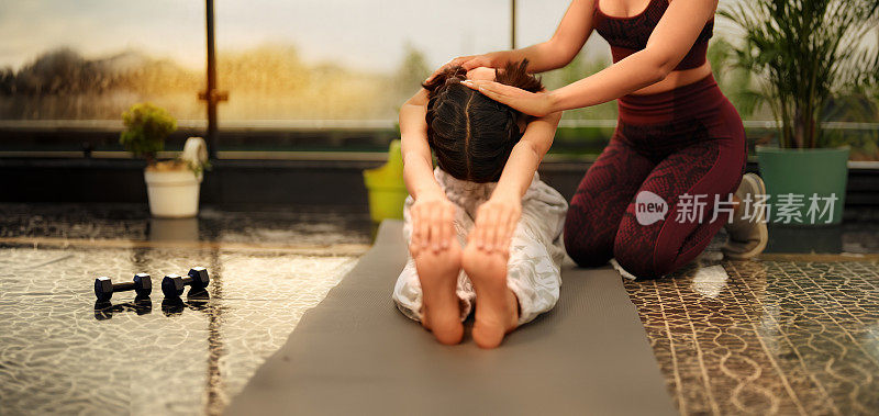 印度印度教快乐美丽的z世代女性穿着运动服坐在垫子上做脚趾触摸瑜伽体式锻炼课程一起在户外的家。两个微笑的青少年运动女性早上拉伸热身运动学习好习惯