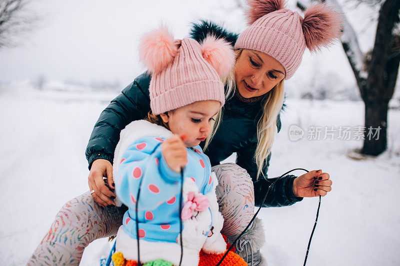 母亲和蹒跚学步的女儿在雪地里玩雪橇