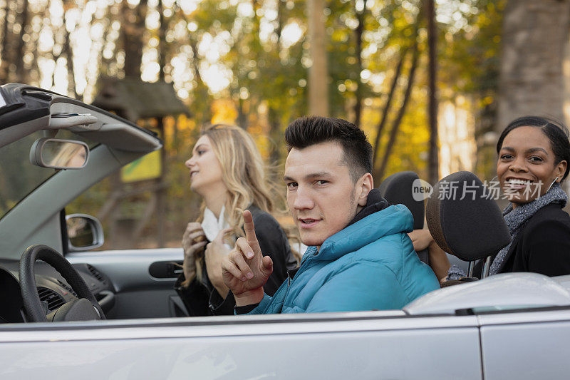 和朋友一起开敞篷车自驾游。一个年轻的男人和两个年轻的女人在车里，一起度过浪漫的时光。