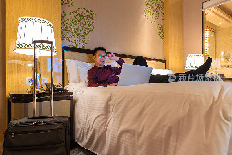 一个商人在酒店房间的床上用笔记本电脑工作