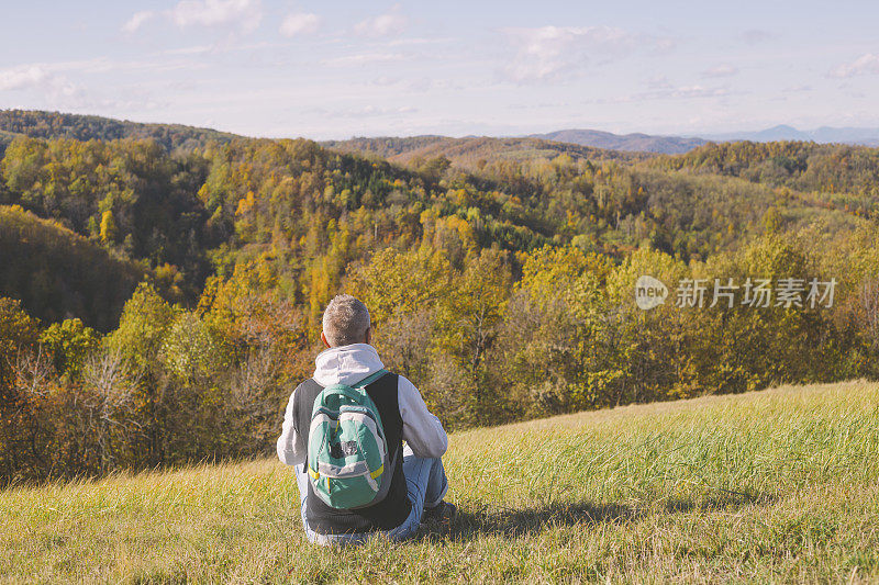 成年男子徒步者坐在草地上在美丽的山区自然在印度夏秋日。