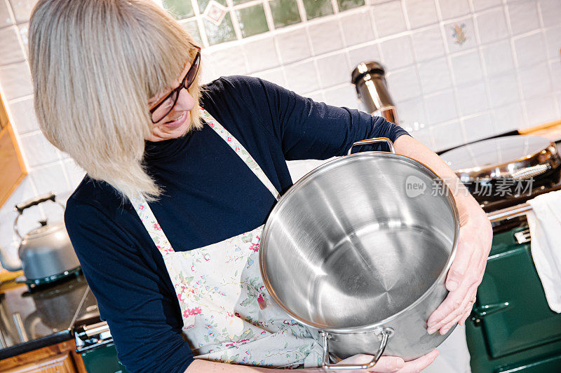 一个女人在厨房里，手里拿着一个大汤锅