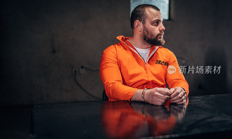 一个囚犯穿着橙色的囚服，独自坐在审讯室里