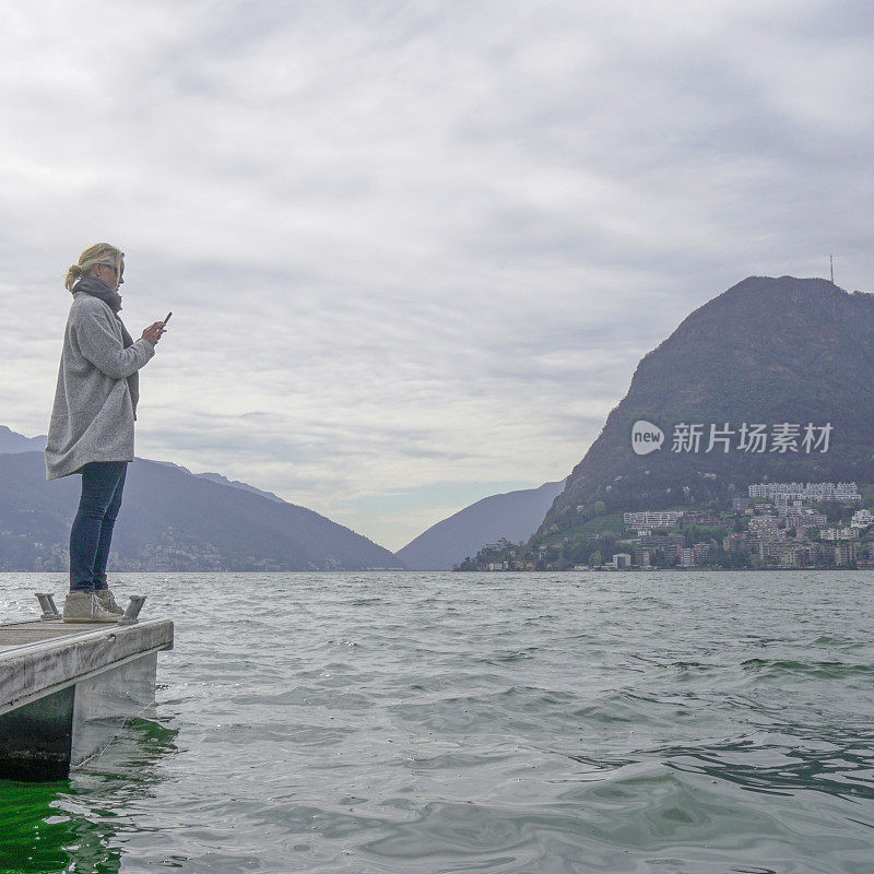 成熟的女人站在湖边的码头上用手机