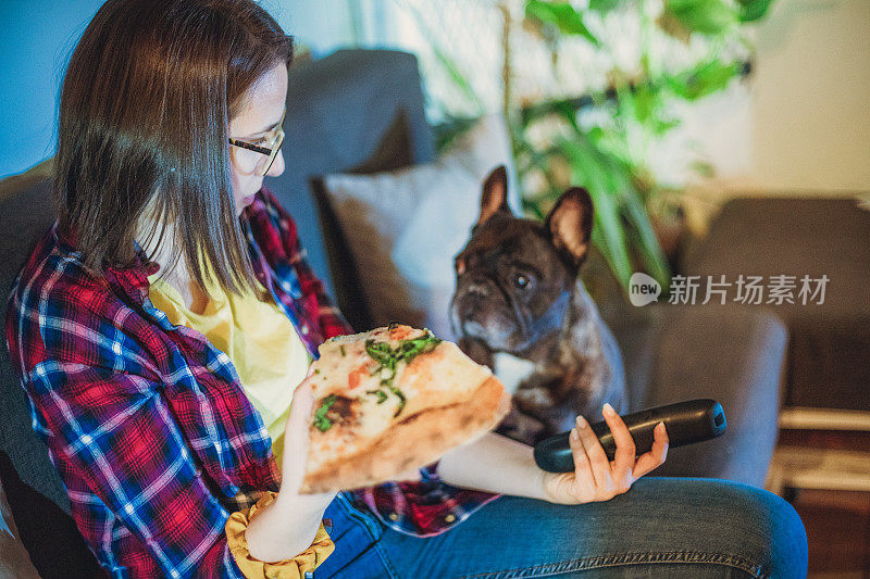 一个女人在沙发上吃披萨，和她的狗一起看电视