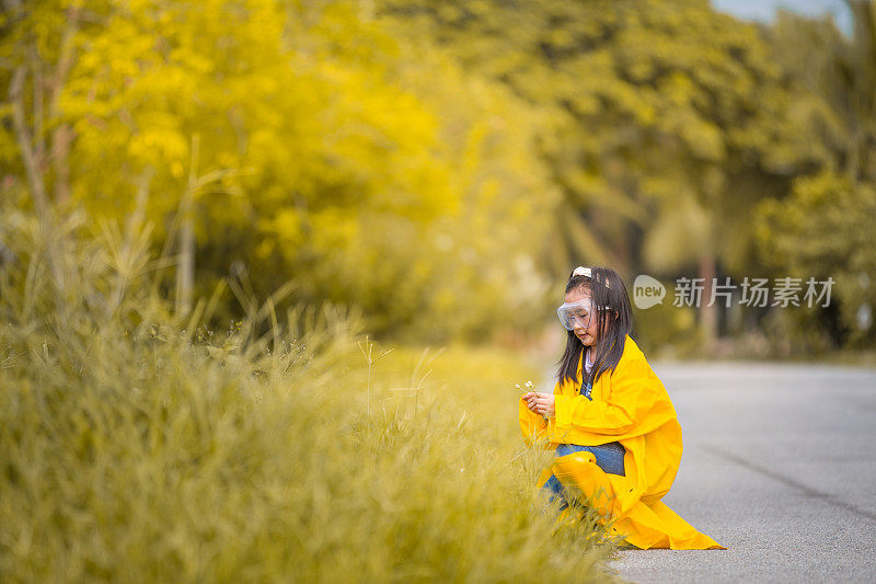 一个亚洲的中国女孩穿着雨衣和农家鞋在农场的草地上玩耍。