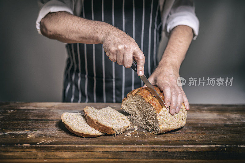 面包师在面包店的木桌上将黑麦面包切成片