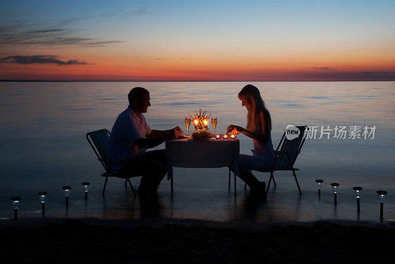 年轻夫妇在海滩上用蜡烛共进浪漫晚餐