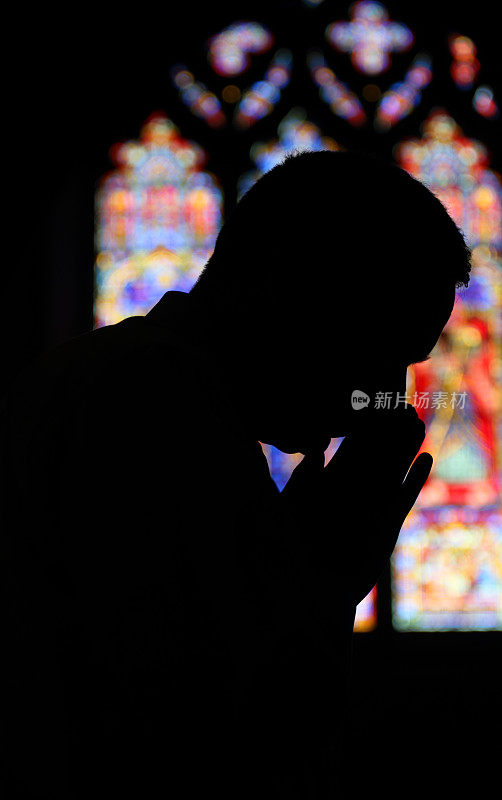 男人在教堂祈祷――彩色玻璃剪影