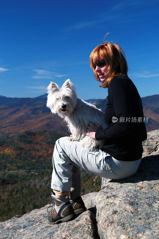 女人徒步旅行和抱着westie狗在山顶