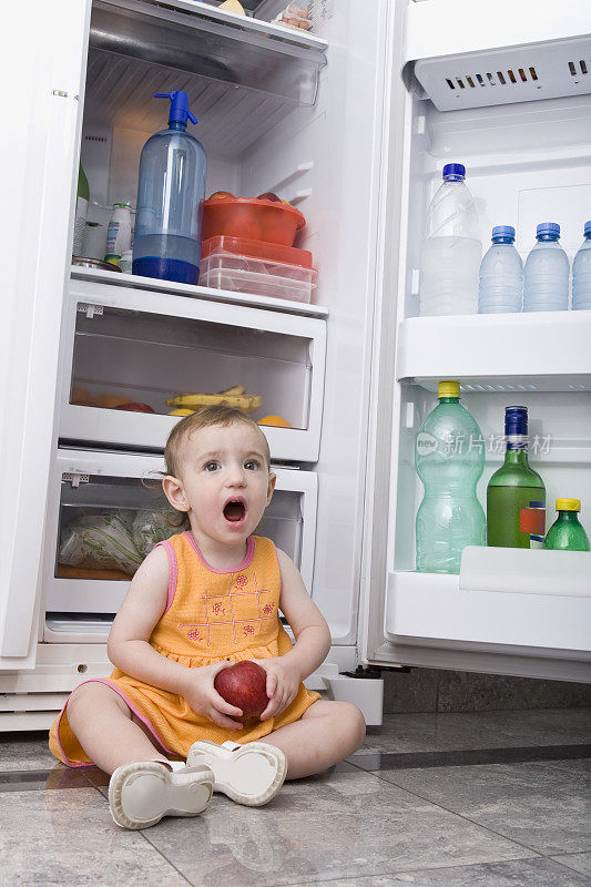 小女孩拿着苹果坐在冰箱前