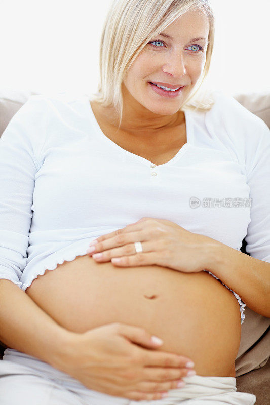 快乐的孕妇抱着她的肚子在家