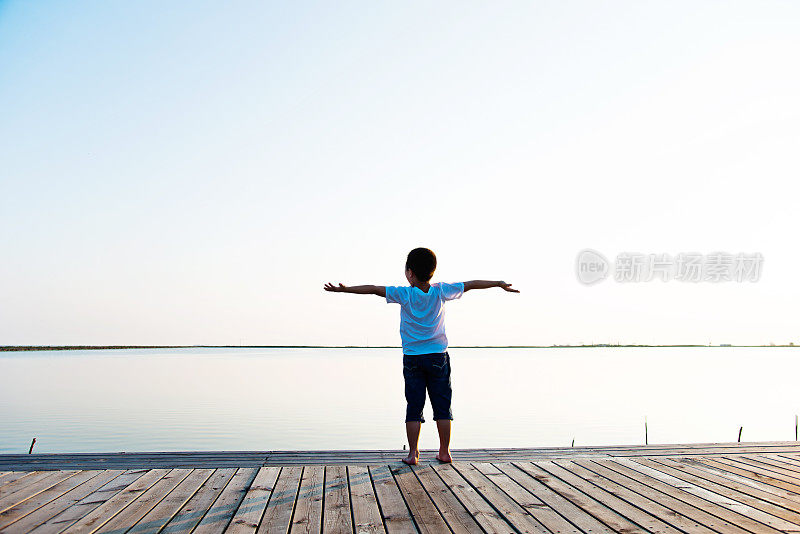 小男孩伸开双臂站在湖边