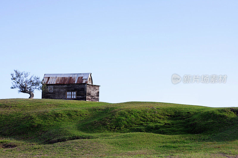 绿树成荫，天空湛蓝的小山上的乡村小屋