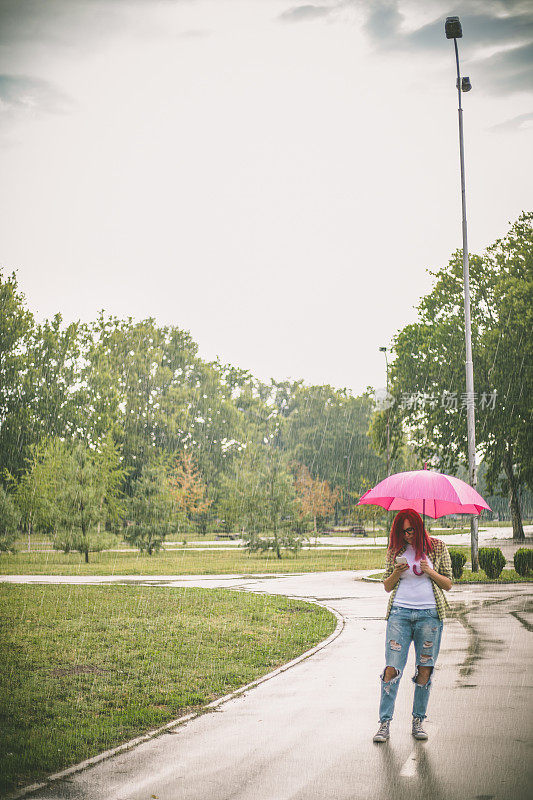 拿着雨伞在街上看手机的女人。